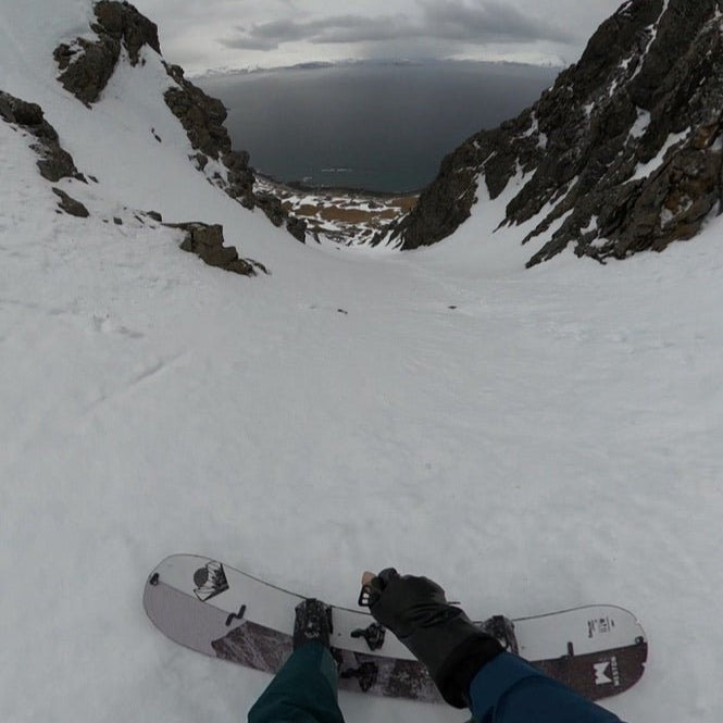 a splitboarder rides with an ice axe in a rock lined couloir above the shorline beach on Russelvfjellet on the northern lyngen peninsula