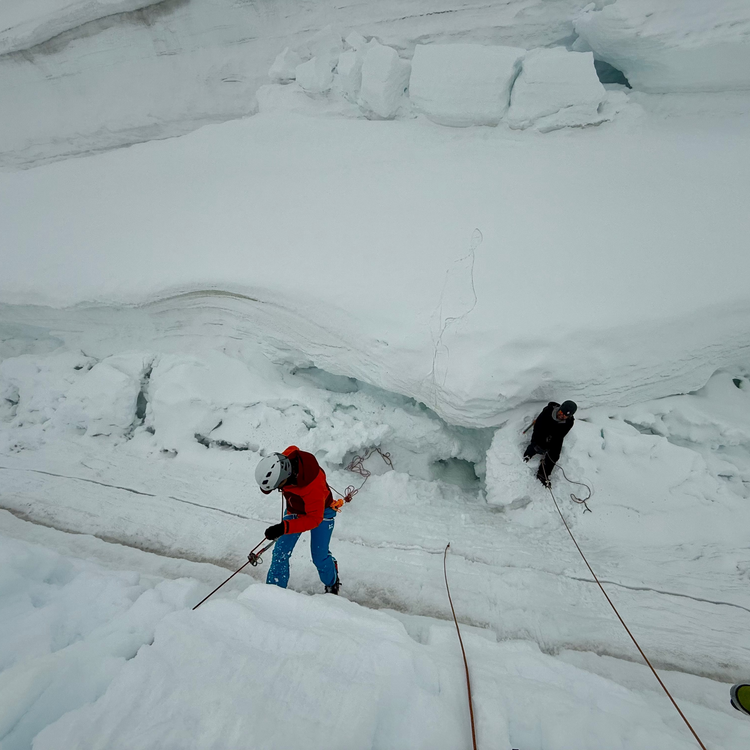 Person in red jacket climbing a snowy mountain with ropes