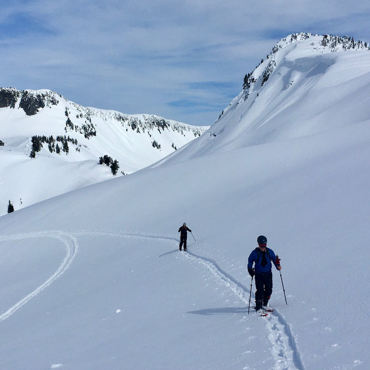 Two backcountry skiers walking in a skin track in the Mount Baker Backcountry. The snow covered basin is pristine with no ski tracks yet to be seen.
