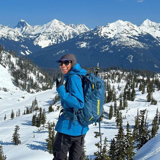 A happy guest turns to wave to the camera while looking out towards American Border peak and the surrounding jagged snow covered peaks.
