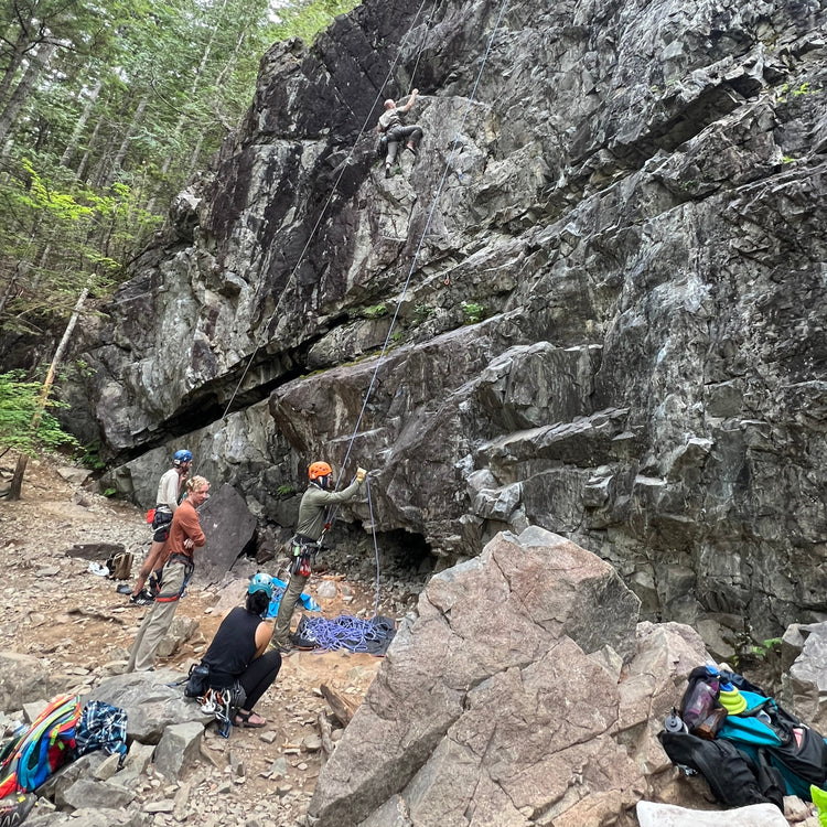 A group of people rock climbing with a rock guide at deception crag at exit 38 north bend wa. Some are top rope climbing higher up the rocks while others are lead climbing lower, resting or preparing to climb.