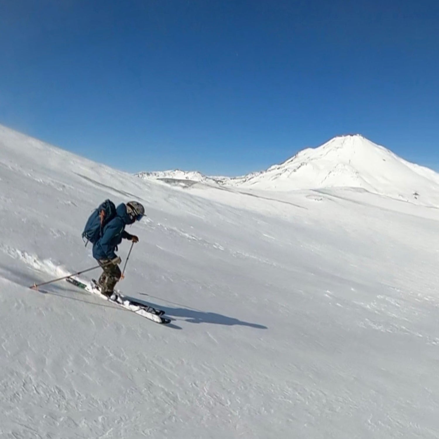 a backcountry skier makes turns on volcan nevados de chillan with volcan chillan in the back ground while using ski lifts from centro de ski nevados de chillan and staying in las trancas chile