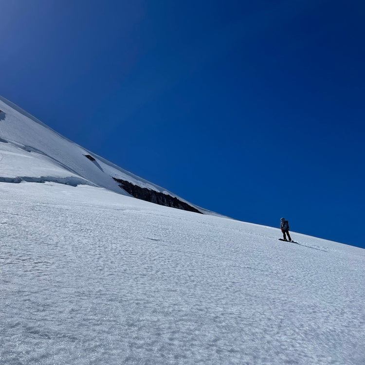 Person standing on a snow-covered mountain slope with clear blue sky