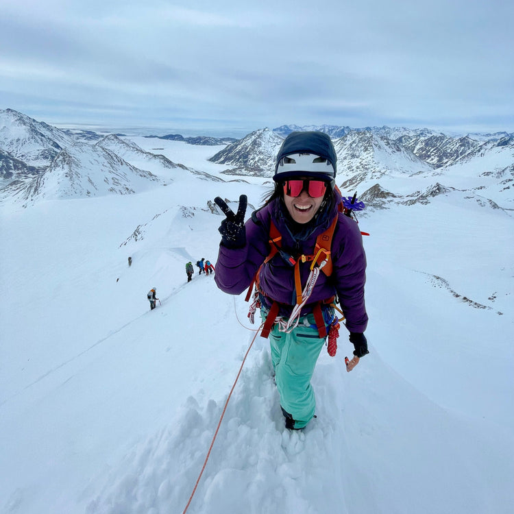 a happy lady giving a peace sign at the summit of a mountain in greenland during a weeklong guided ski trip on the east coast of greenland