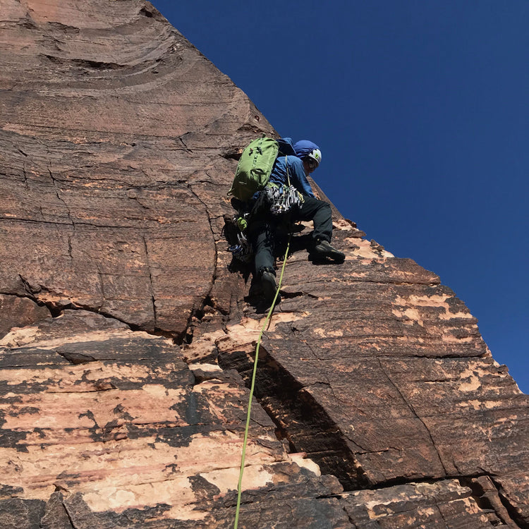 A guide moves up a rust red slab of rock.