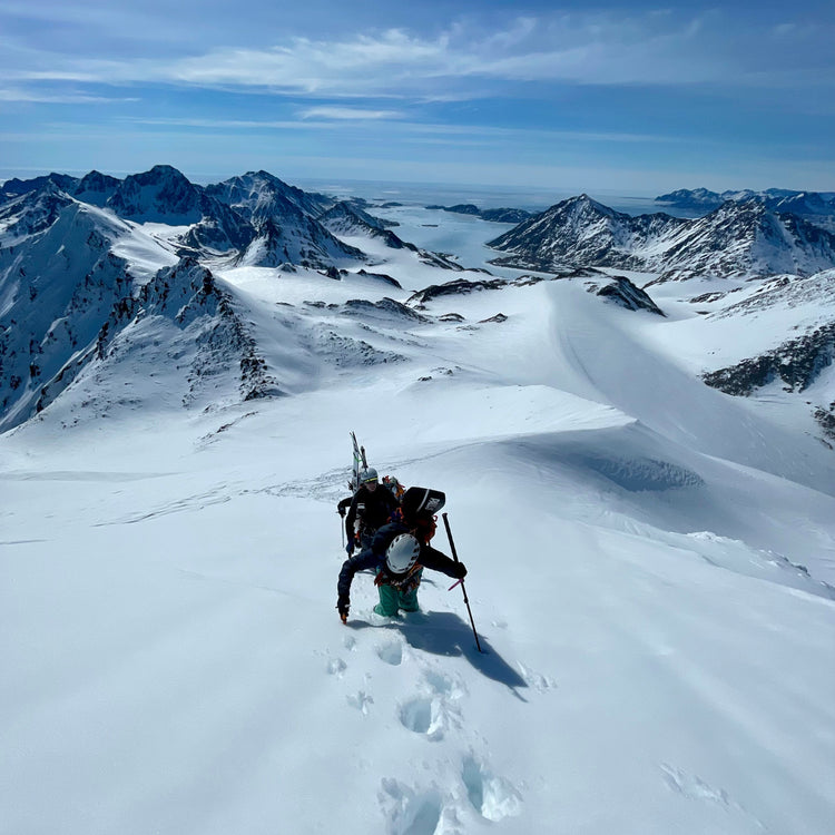 during a weeklong guided trip skiers bootpack a snowy mountain on the east coast of greenland with a frozen fjord and the north atlantic in the distance