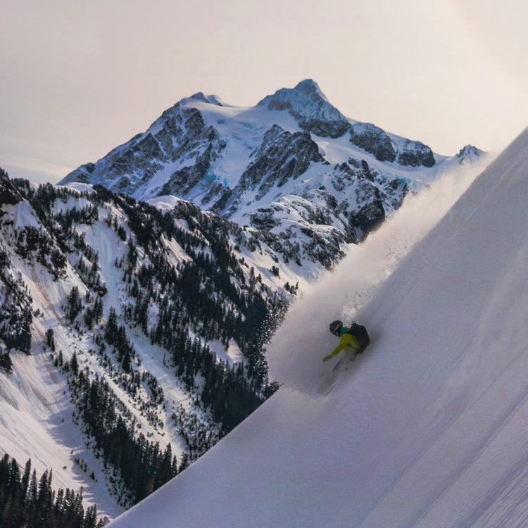 Splitboarder at the Mount Baker Splitfest taking a deep powder turn down a steep slope. In the background Mount Shuksan is an iconic and dramatic mass of rock, ice, and snow.