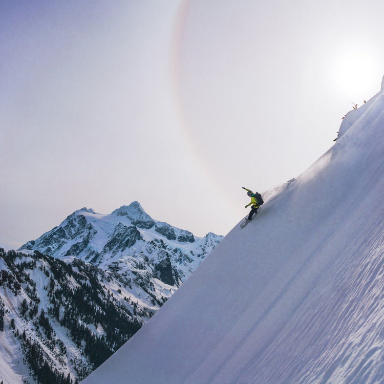 Another shot of a splitboarder making a big arching turn down a steep snowy face with Mount Shuksan in the background.