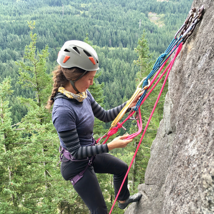 A climber practices rock rescue systems while standing at a n anchor high above an emerald green forest in north bend washington