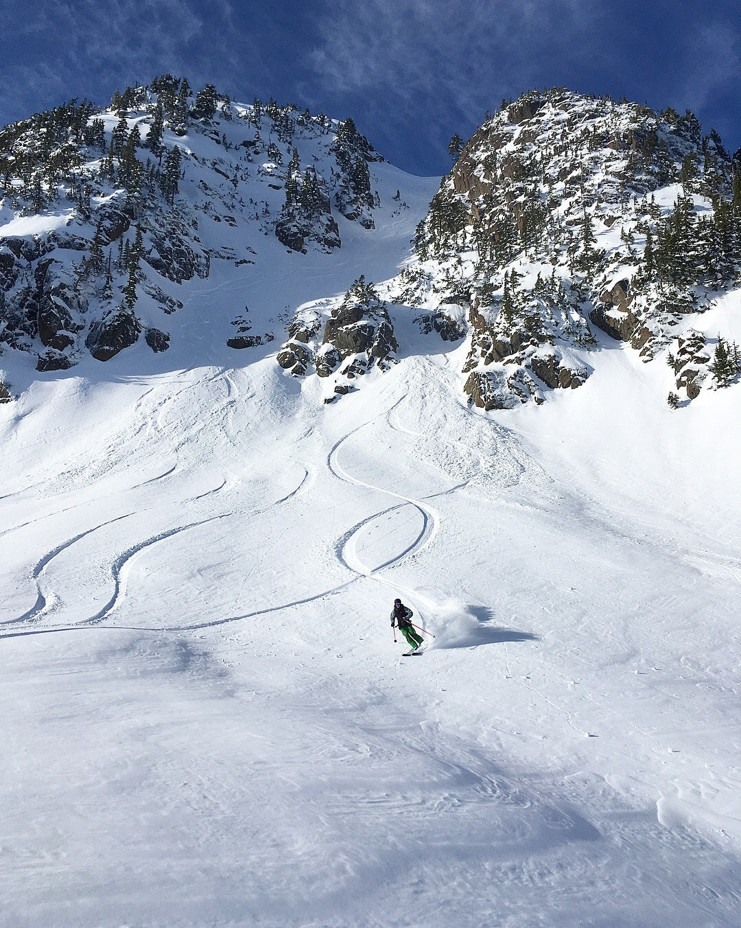 Skier coming out of a rocky chute making big open turns in powder. 