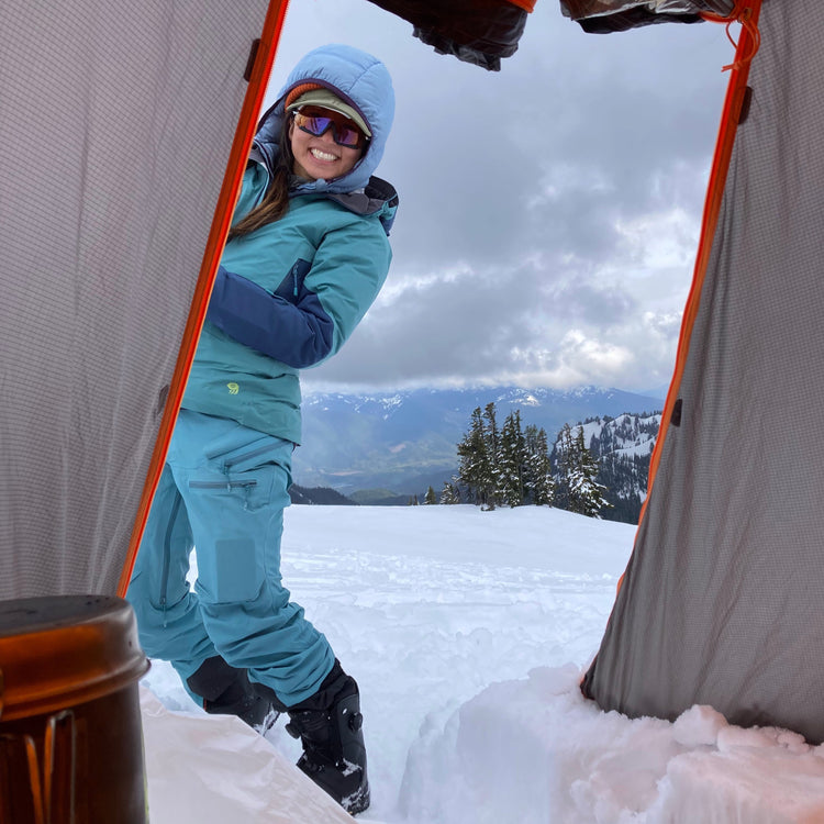 summer snowboard camp views from the tent with a happy female splitboarder smiling in the doorway while camping on the squak glacier
