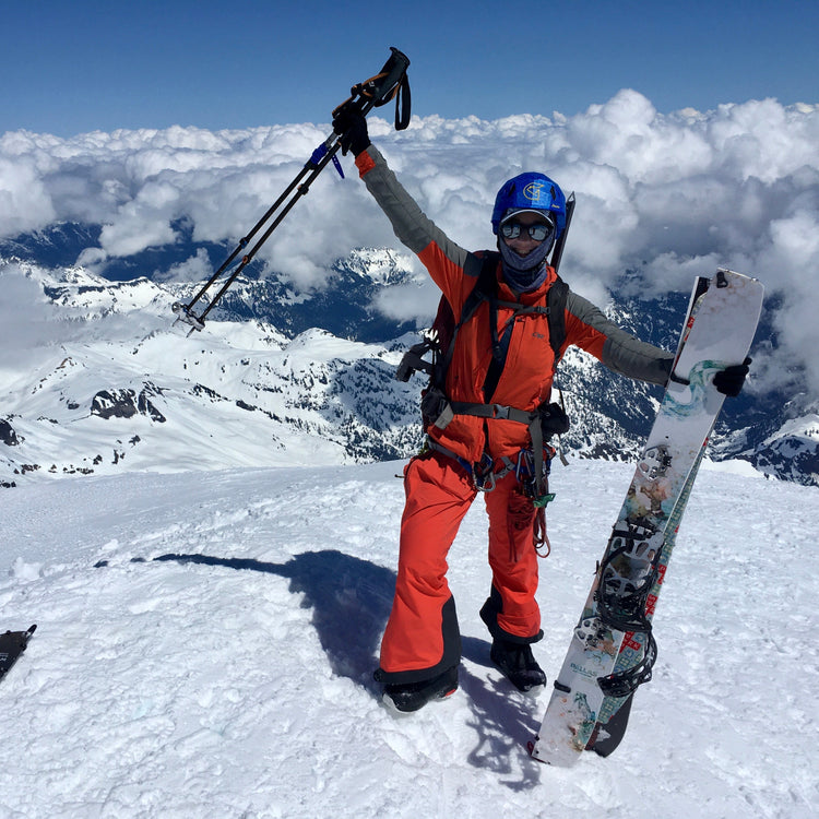 on the 10,781' summit of mt baker a womens splitboarder celebrates holding her pallas splitboards with puffy clouds and mount baker ski area in the background