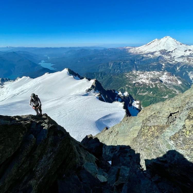 a climber on the se rib of mount shuksan above the sulphide glacier after climbing the fisher chimney route with mount baker, park glacier, boulder glacier