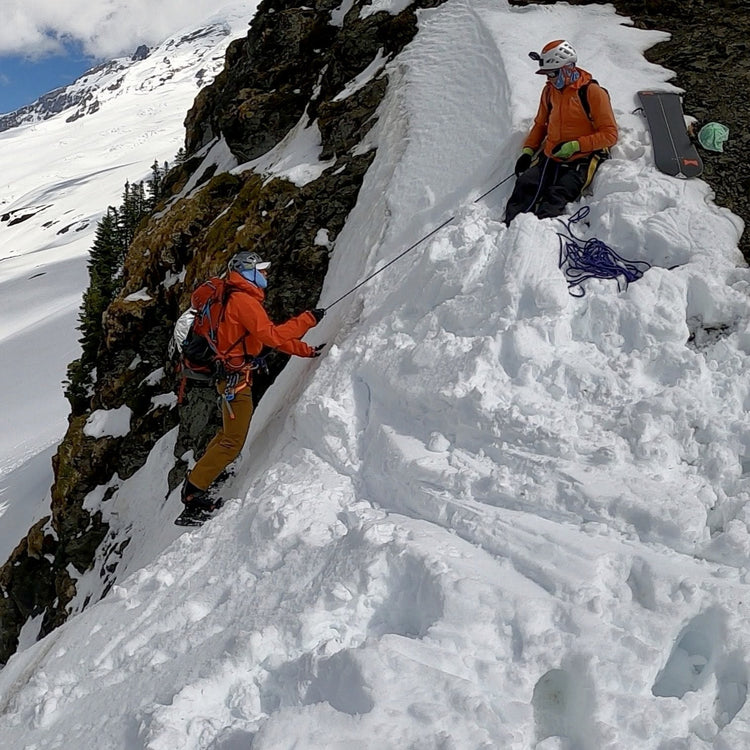 a snowboarder gives a hip belay for a splitboarder riding on belay during a splitboard mountaineering course on mt baker