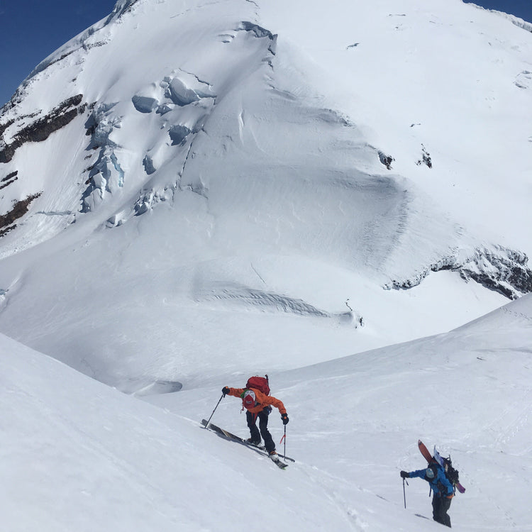 Mount Baker looms over a skier and snowboarder while ascending Colfax Peak.
