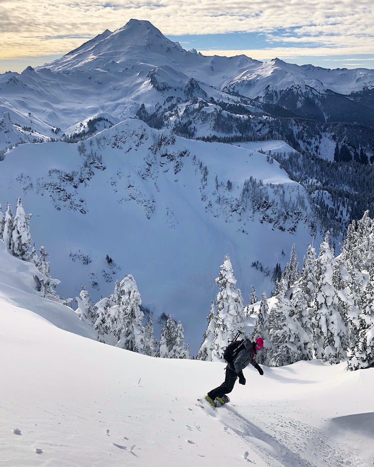 Snowboarding in the Mount Baler backcountry is a beautiful experience. A snowboarder rides in the sunshine with Mount Baker in the background.