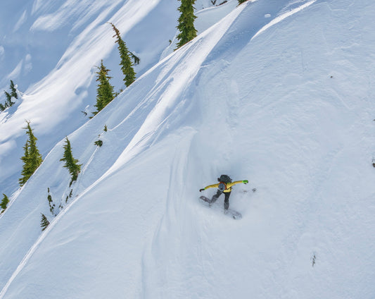 a snowboarder rides through steep terrain next to a wind sculpted drift
