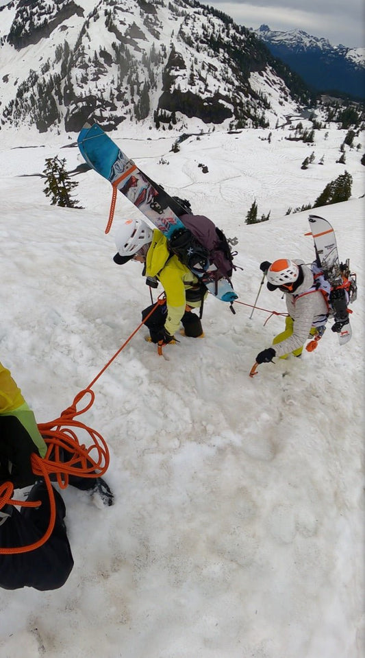 splitboarders hike up a snow slope at mount baker while being roped with a guide at mount baker