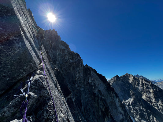 Mountain guide leads up a crack on the fin of dragontail peak with the sun shining above
