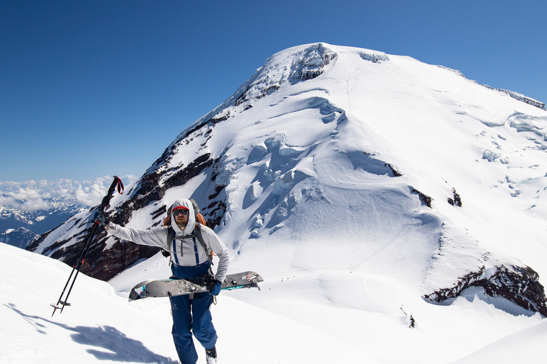 splitboarder hikes with the glaciated summit of mount baker, kulshan, behind