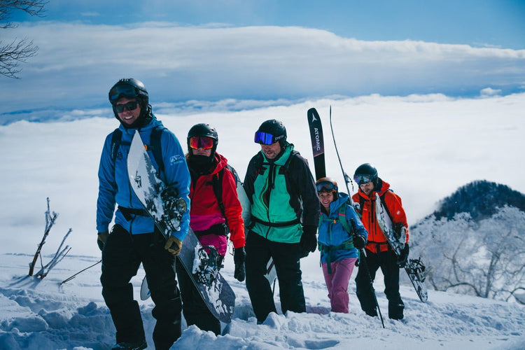 a group of skiers and splitboarders hike through the snow above the clouds with their ski guide in furano hokkaido japan