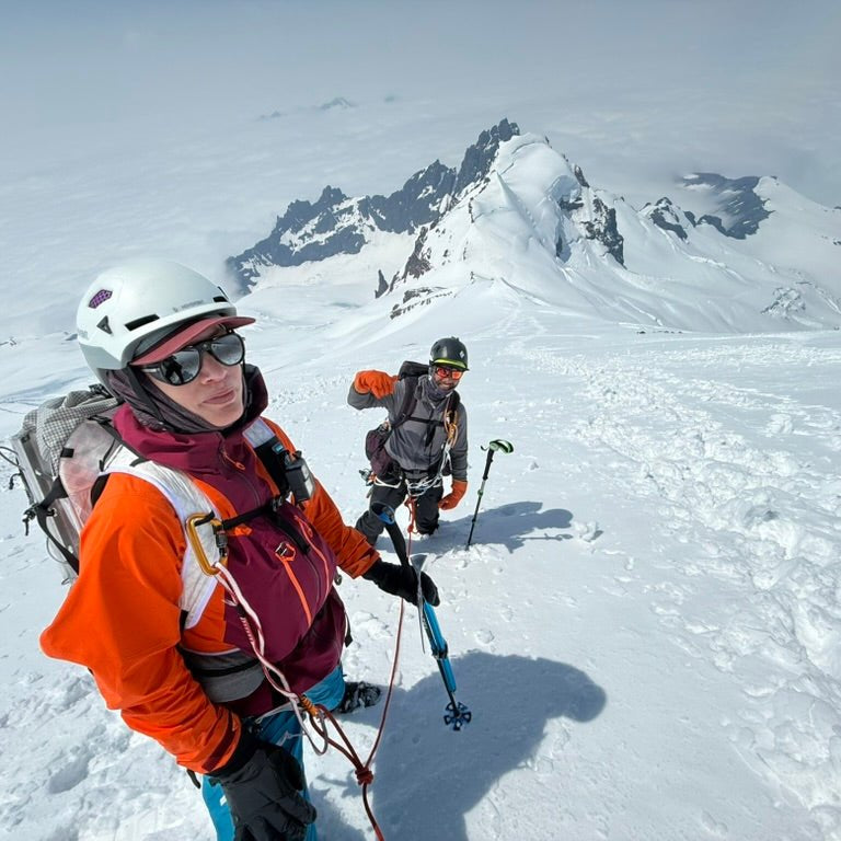 Two climbers on a snowy mountain with backpacks and helmets.