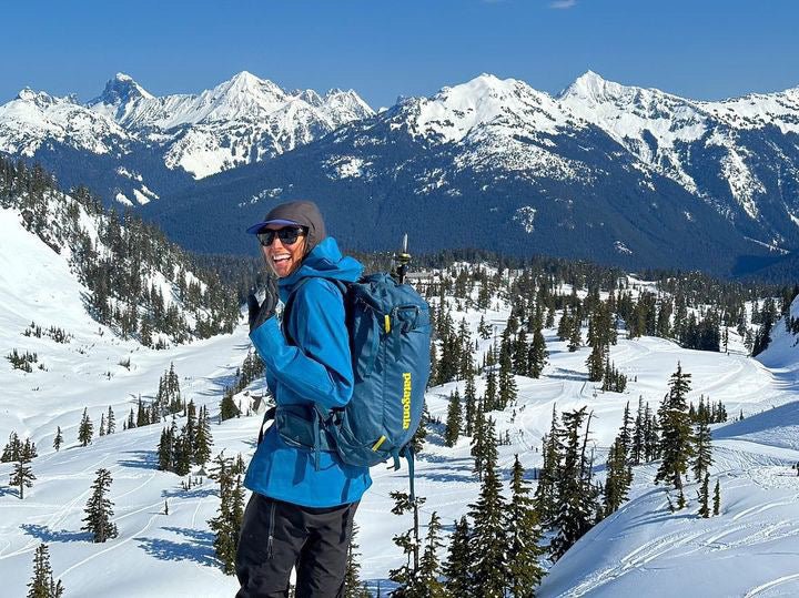 A happy guest turns to wave to the camera while looking out towards American Border peak and the surrounding jagged snow covered peaks. 