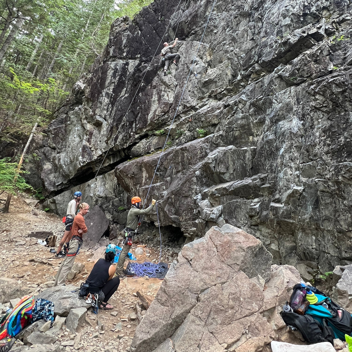 A group of people rock climbing with a rock guide at deception crag at exit 38 north bend wa. Some are top rope climbing higher up the rocks while others are lead climbing lower, resting or preparing to climb.