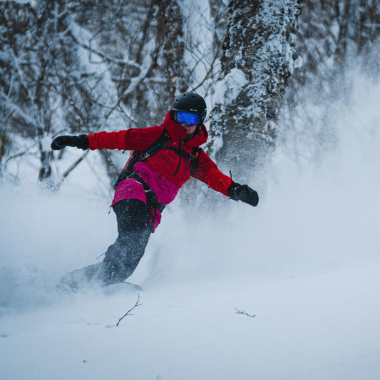 a rider sprays powder snow while making a turn with arms out in the birch trees during a ski guide trip in niseko japan