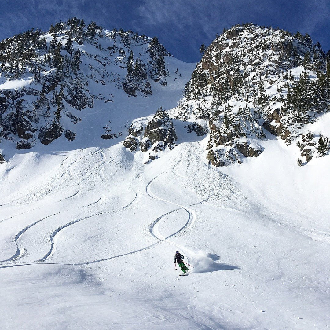 Skier coming out of a rocky chute making big open turns in powder. 
