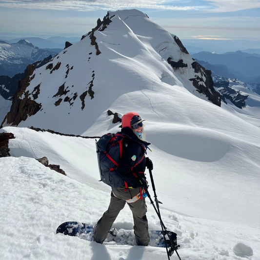 Splitboard Guide Sarah Macgregor is stopped and smiling with poles on her weston womens splitboards on the coleman glacier on mt baker with colfax peak and icefall in the background during guided exposures 4 day splitboard mountaineering course