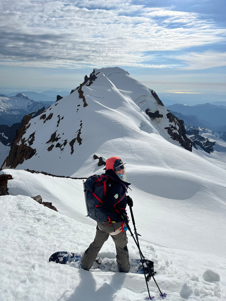 Splitboard Guide Sarah Macgregor is stopped and smiling with poles on her splitboard on the coleman glacier on mount baker with colfax peak and icefall in the background