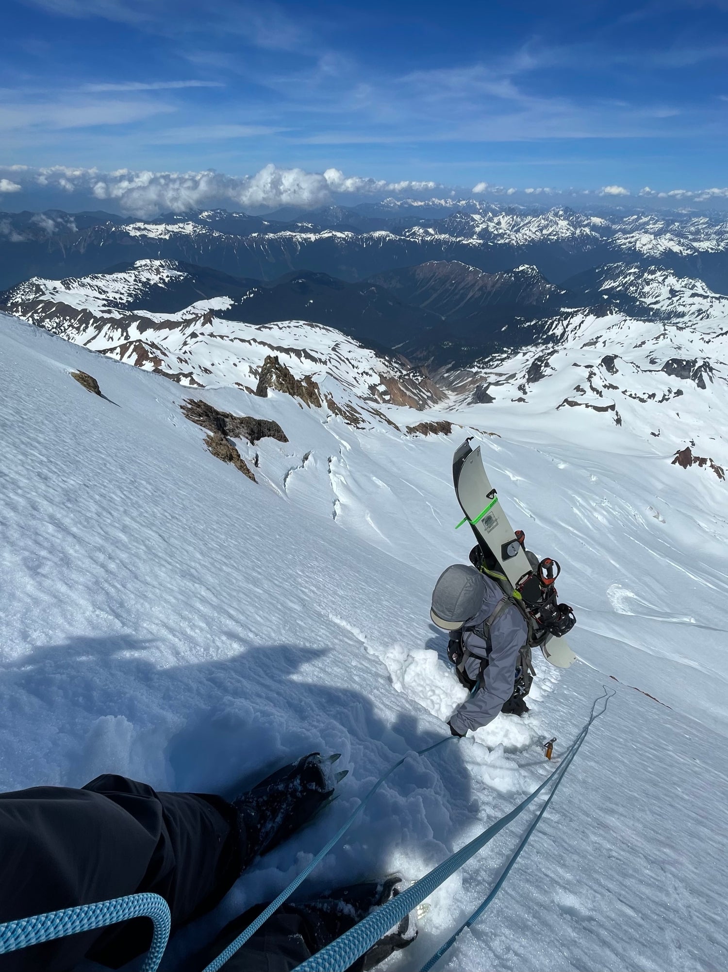 On the steepest section climbing Mount Baker, with splitboard A-framed on pack, we get comfortable using a rope and crampons. Blue skies and Mountain views in the background. 