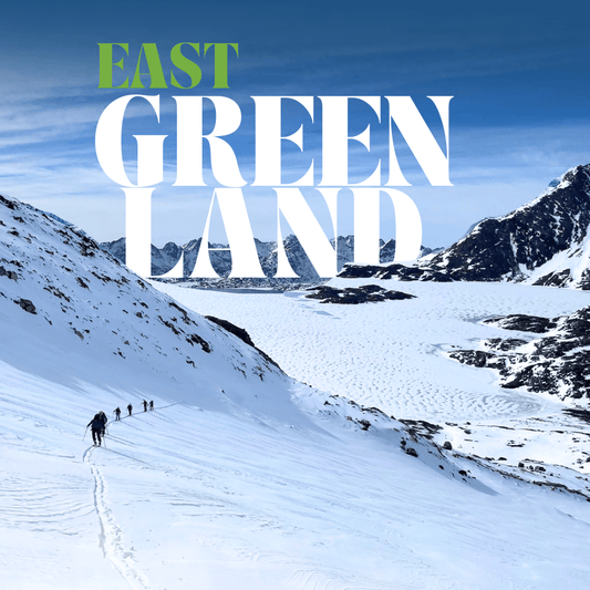 Snowy mountain landscape with skiers and East Greenland on a blue sky background