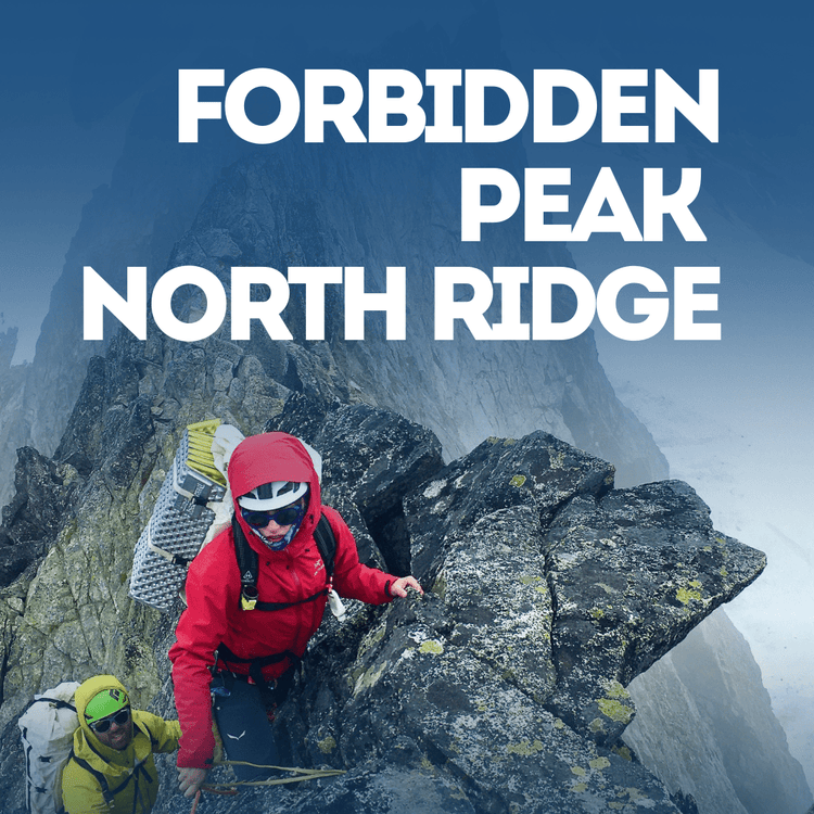 Two climbers on a rocky mountain peak with Forbidden Peak North Ridge
