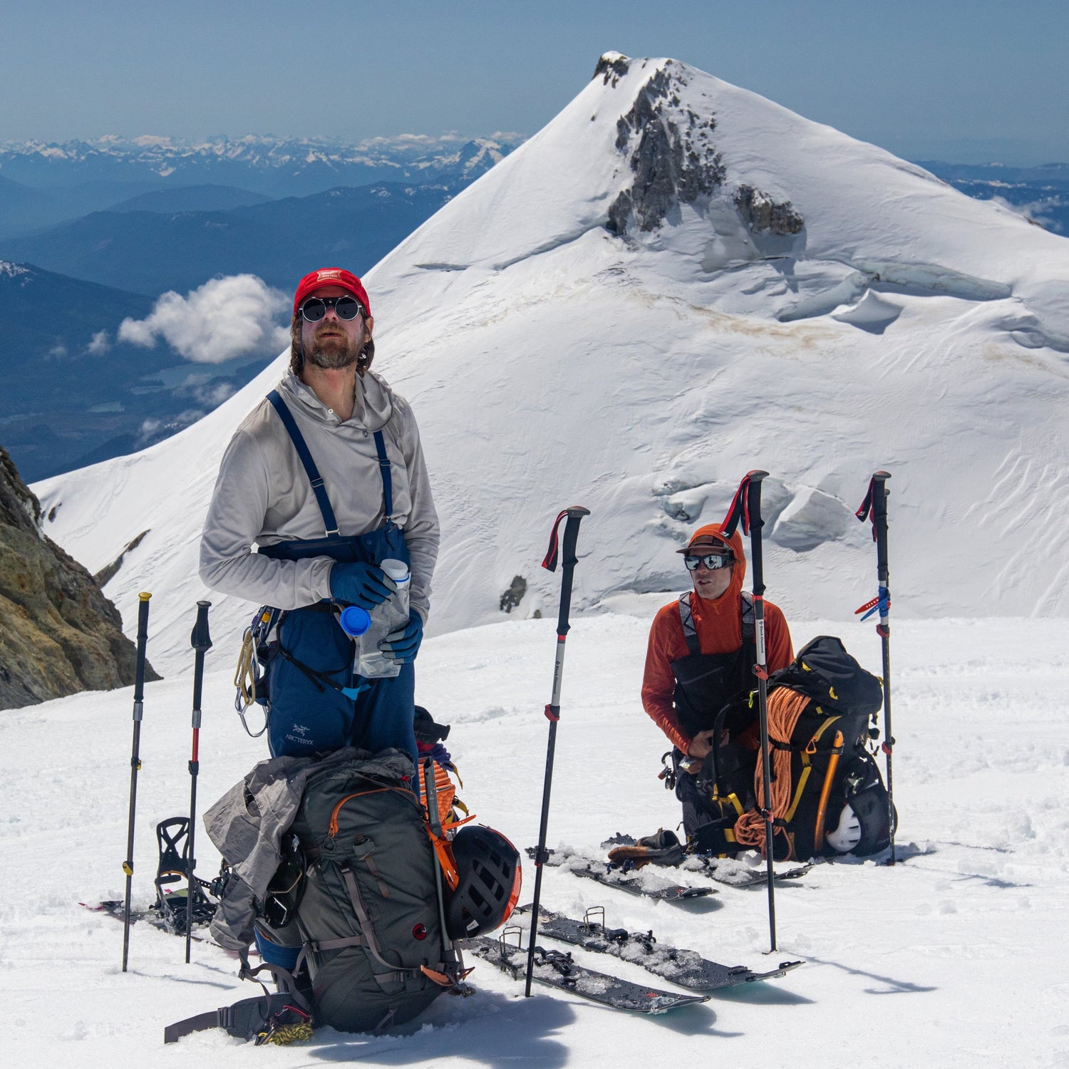 Two skiers on a snowy mountain with backpacks and ski equipment.