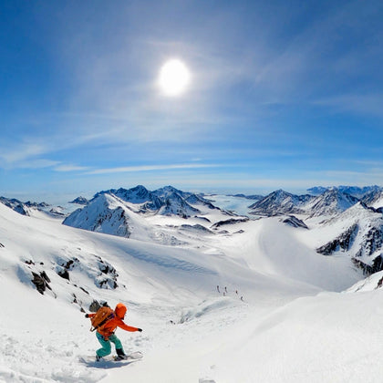 a women splitboarder rides a mountain near kulusuk east greenland with the arctic sun overhead, a frozen fjord below, a tidewater glacier, and the north atlantic in the distance during a guide trip