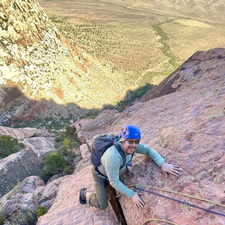 A guided climber tops out a sandstone route with the Red Rock Canyon valley below, Nevada