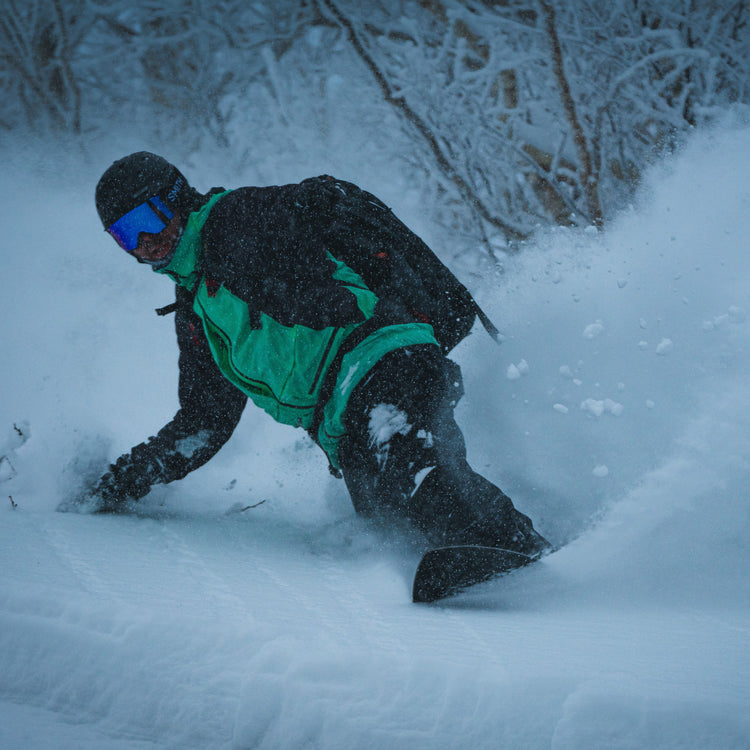 a snowboarder takes a toeside turn sparying snow on a ski guide trip in furano hokkaido japan