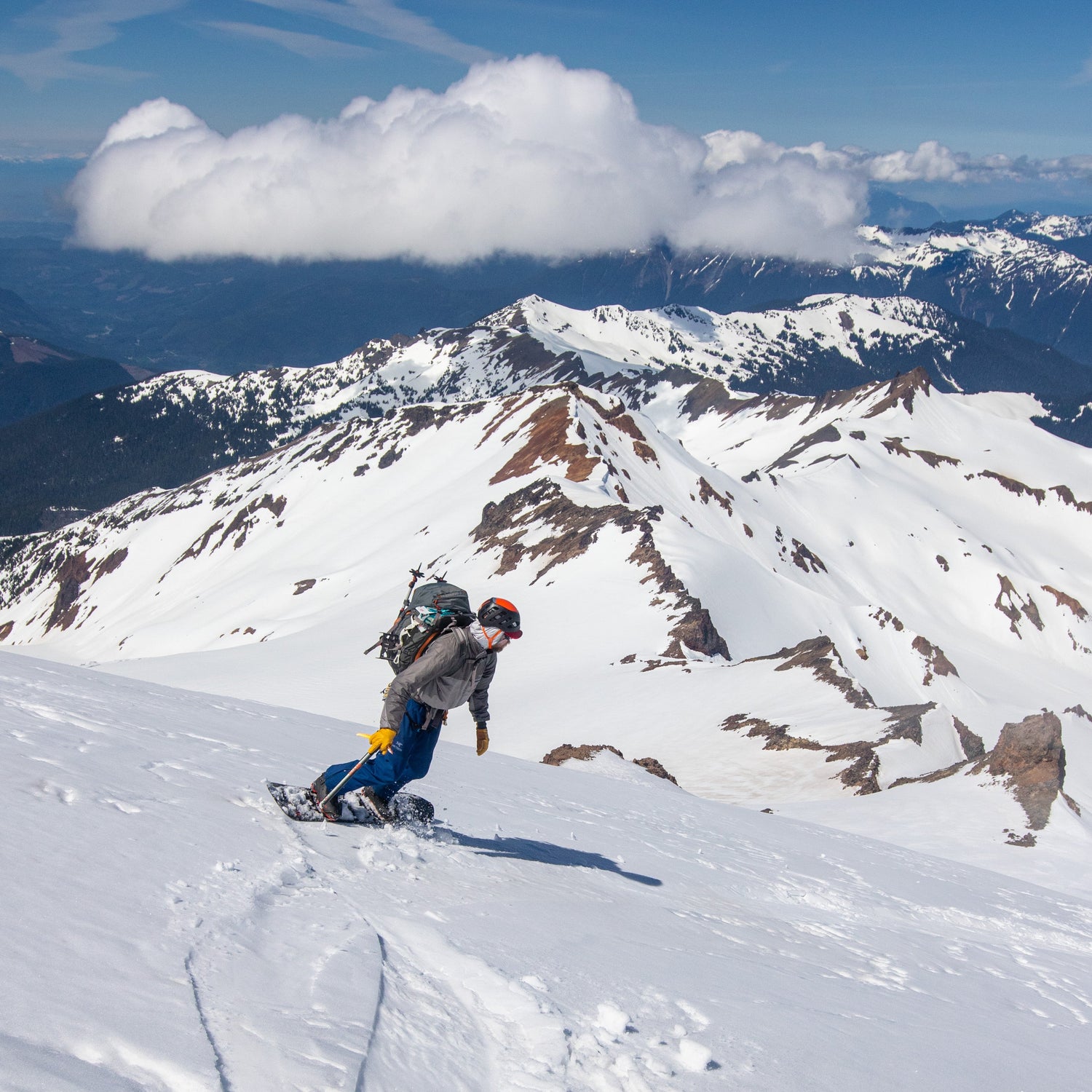 splitboard mountaineer riding with an ice axe on the mazama glacier mt baker with clouds above a snowy springtime skyline divide 