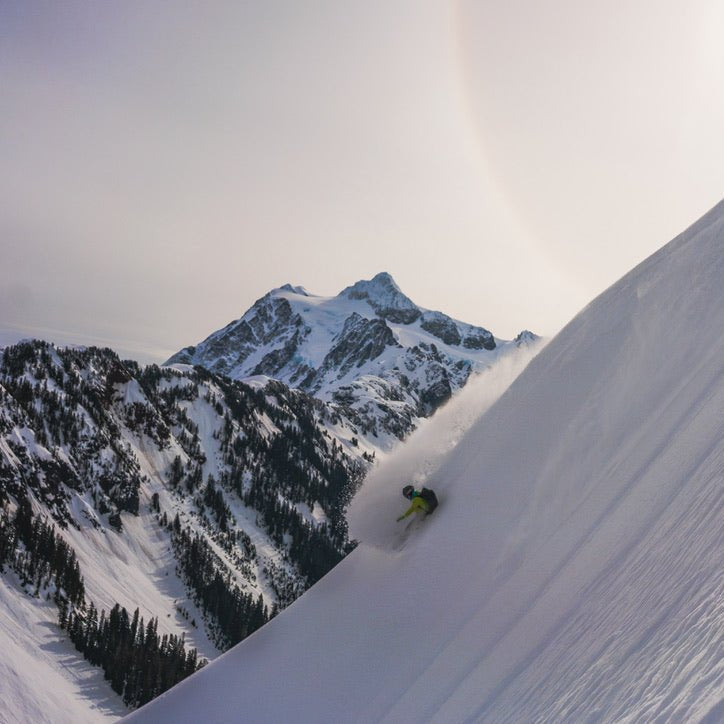 snowboarder makes a powder turn at artist point and mt baker with mount shuksan, white salmon, hanging glacier, and the mt baker ski area behind