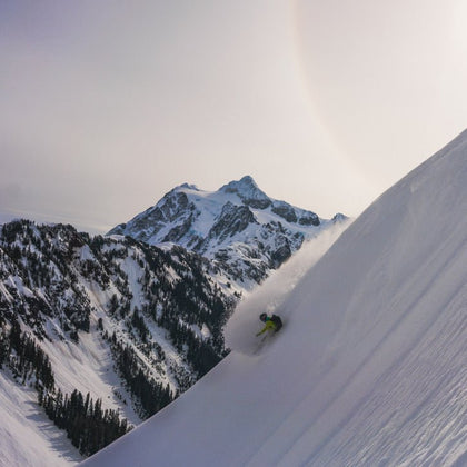 snowboarder makes a powder turn at artist point and mt baker with mount shuksan, white salmon, hanging glacier, and the mt baker ski area behind