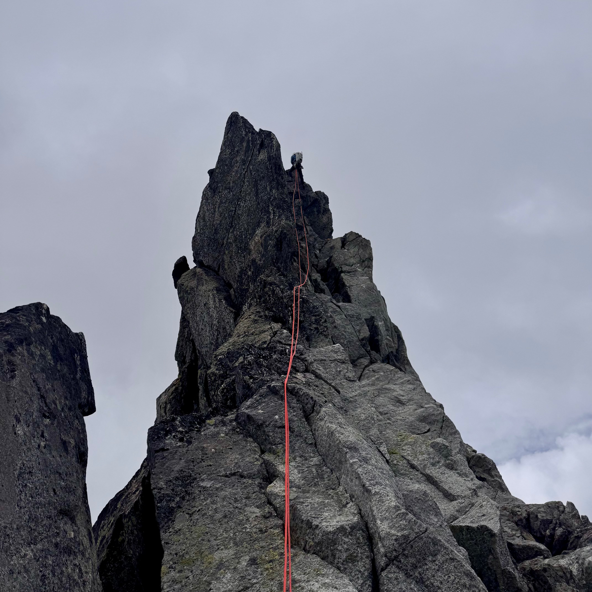 A climber on a rock pinnacle with the rope trailing below on the Torment–Forbidden Traverse