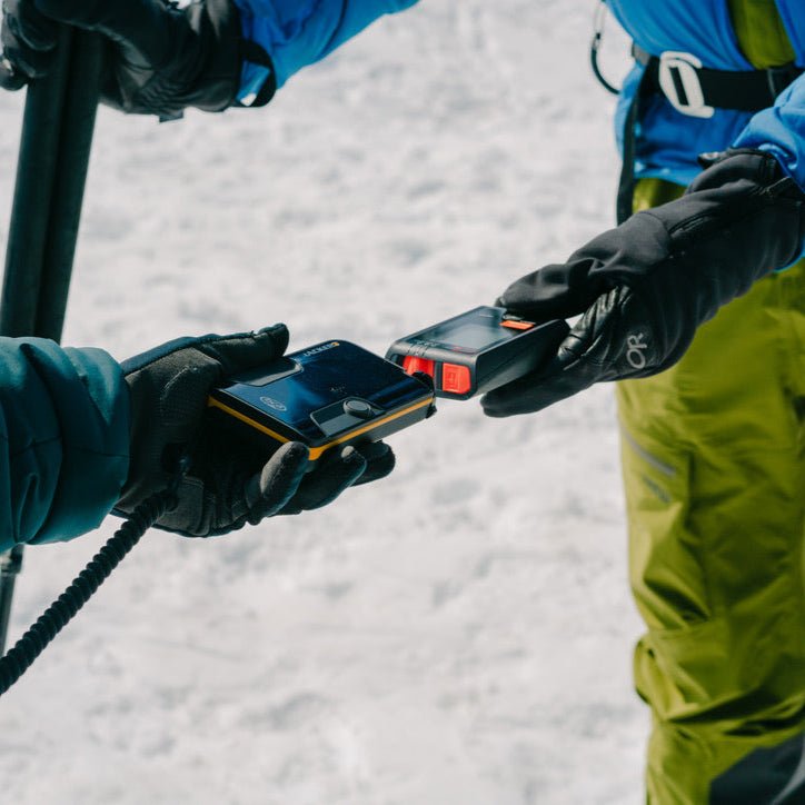 Two skiers handing off an avalanche transceiver in a beacon drill during a women's AIARE avalanche rescue course