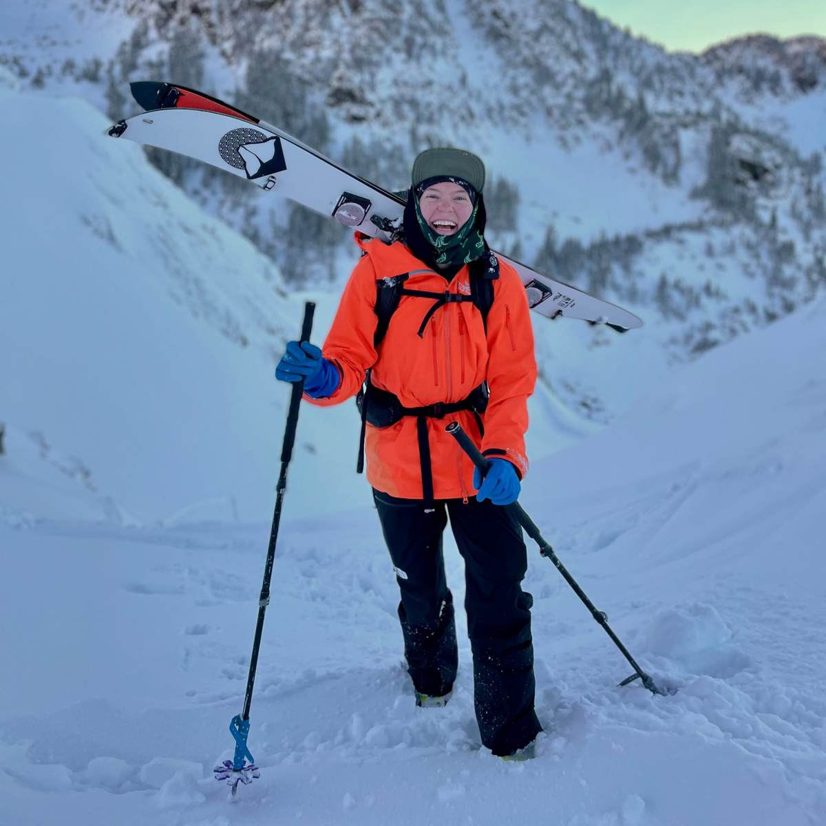 Woman skier in an orange jacket holding her skis on a snowy Mount Baker slope at dusk during a women's intro to backcountry touring course