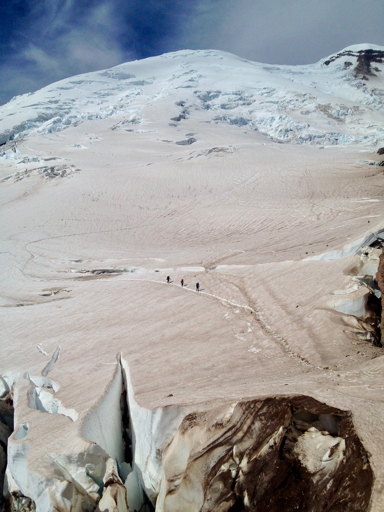 The scale of mount rainier hovers over tiny climbers on the Emmons glacier
