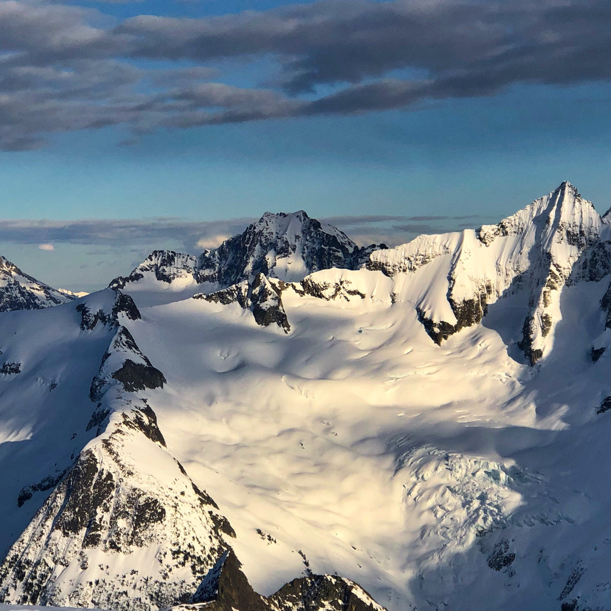 Sunoight shines across the Forbidden Glacier, North Ridge of Forbidden, and the NW Face of Forbidden with Mount Buckner behind with in North Cascades National Park during a forbidden tour ski traverse in washington state