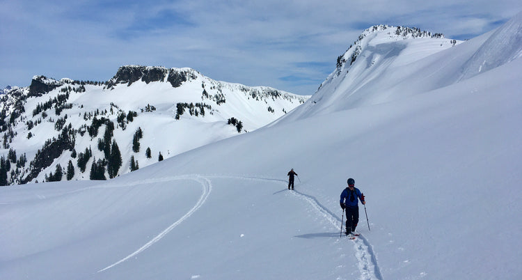 Two backcountry skiers walking in a skin track in the Mount Baker Backcountry. The snow covered basin is pristine with no ski tracks yet to be seen.