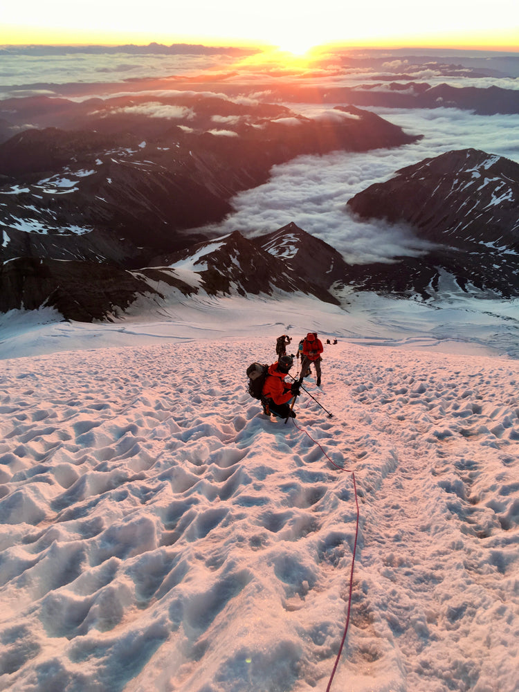 clouds fill the valley below climbers at sunrise in mount rainier national park