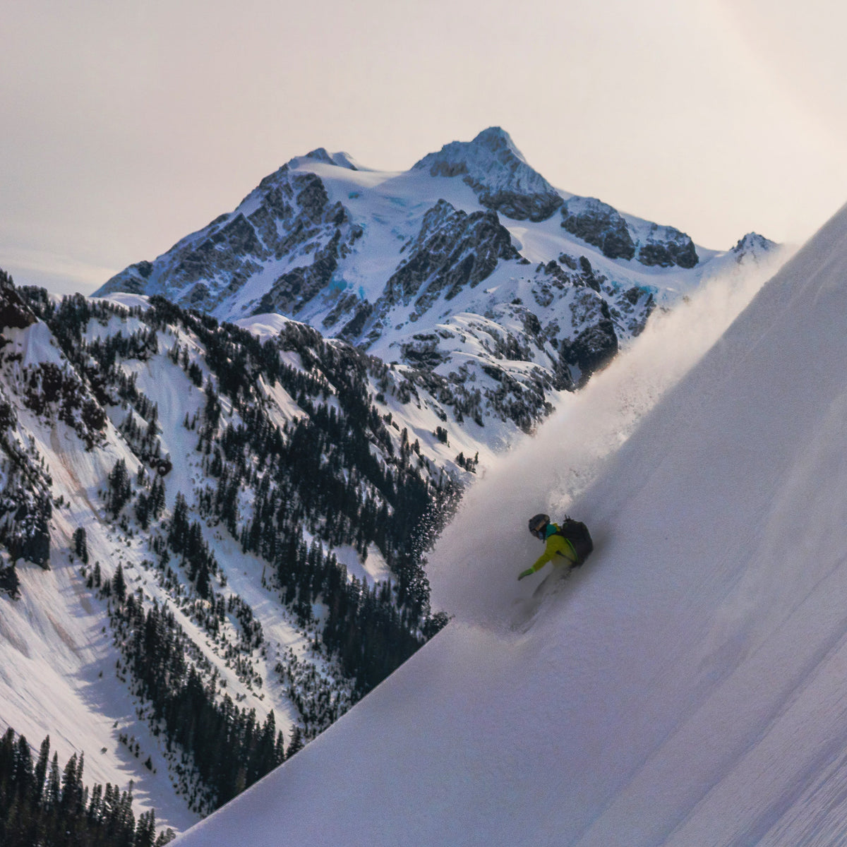 Splitboarder at the Mount Baker Splitfest taking a deep powder turn down a steep slope. In the background Mount Shuksan is an iconic and dramatic mass of rock, ice, and snow.  